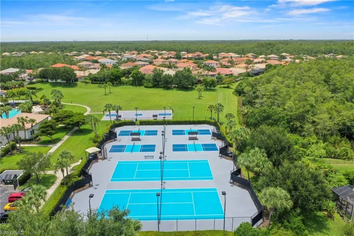 Aerial perspective showcasing multiple tennis courts, pickleball courts, manicured green spaces, and surrounding residential structures with tile roofs