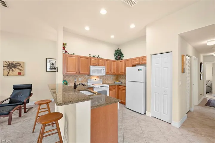 Kitchen featuring a breakfast bar with stone countertop, wood cabinetry, tile backsplash, and recessed lighting