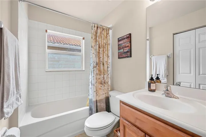 Full bathroom featuring a white bathtub with tile surround, a built-in window, a toilet, and a vanity with an integrated sink and wood-finish cabinetry