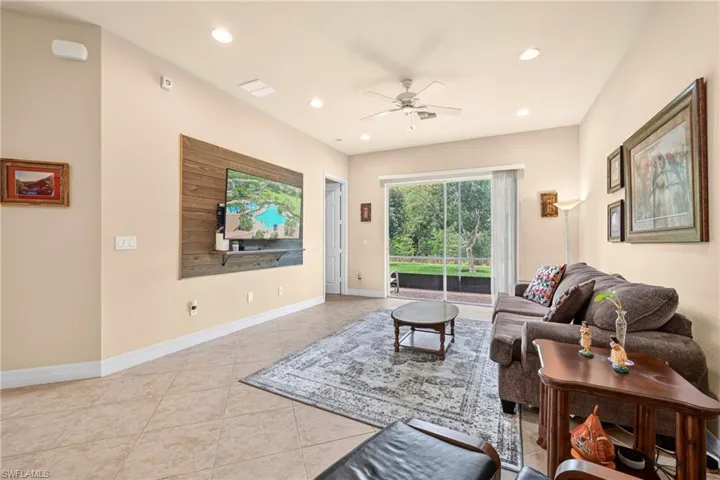 Spacious living area featuring tile flooring, a decorative wood-panel accent wall, recessed lighting, and a ceiling fan