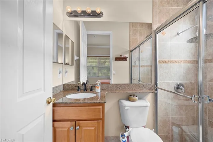 Bathroom featuring a tile-surround shower with glass enclosure, wood-finish vanity with granite countertop, integrated sink, and wall-mounted mirror