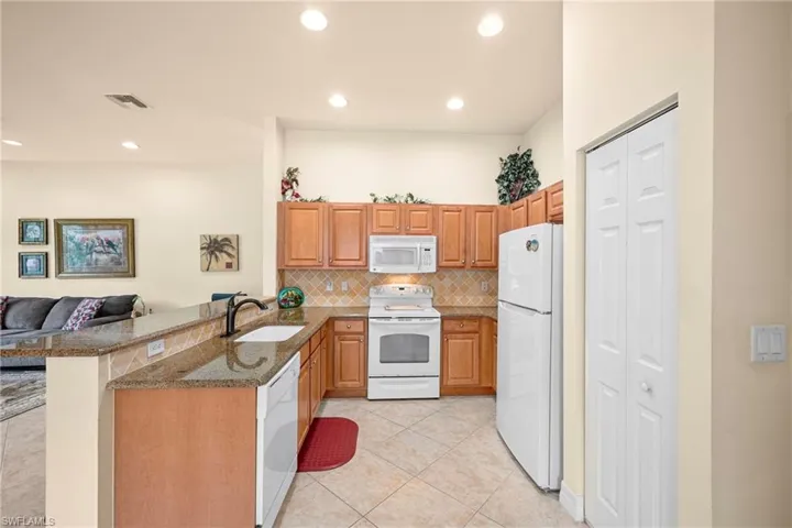 Kitchen featuring granite countertops, wood cabinetry, tile flooring, white appliances, and recessed lighting