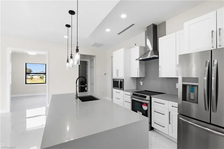 Kitchen with stainless steel appliances, white cabinets, pendant lighting, an island with sink, and light marble finish flooring