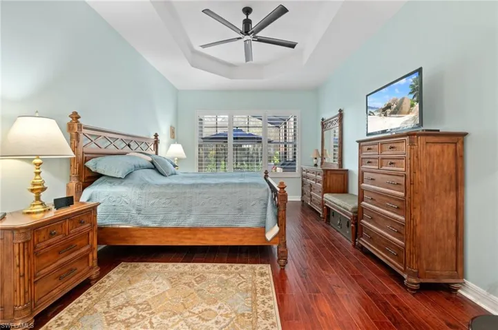 Master Bedroom with detailed ceilings, hardwood floors, and soft color - offering a view of the pool and wooded area beyond.