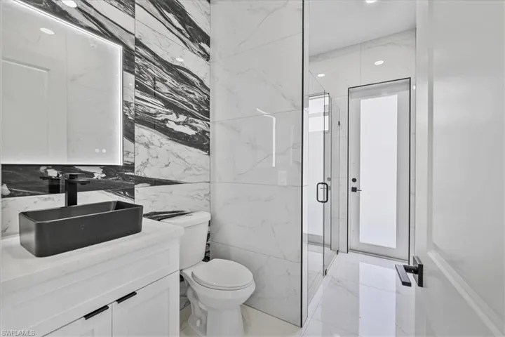 Bathroom featuring vanity, tile walls, a marble finish shower, and recessed lighting