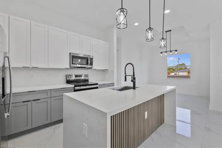 Kitchen featuring recessed lighting, decorative light fixtures, stainless steel appliances, gray cabinets, and light stone countertops