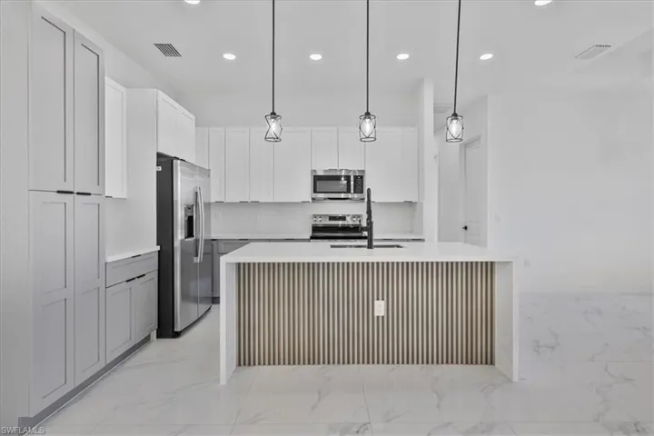 Kitchen with appliances with stainless steel finishes, hanging light fixtures, light stone counters, and recessed lighting