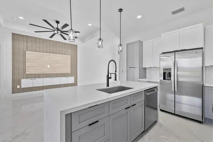 Kitchen featuring gray cabinetry, appliances with stainless steel finishes, light marble finish floors, light stone counters, and recessed lighting