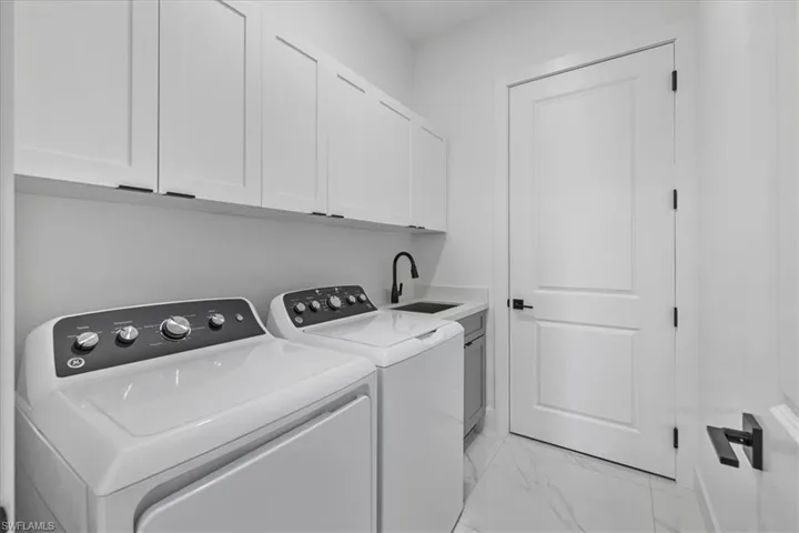 Washroom featuring cabinet space, washer and dryer, and light marble finish flooring