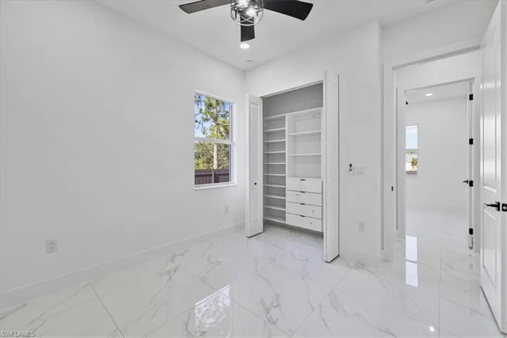 Unfurnished bedroom featuring a closet, multiple windows, ceiling fan, light marble finish floors, and recessed lighting