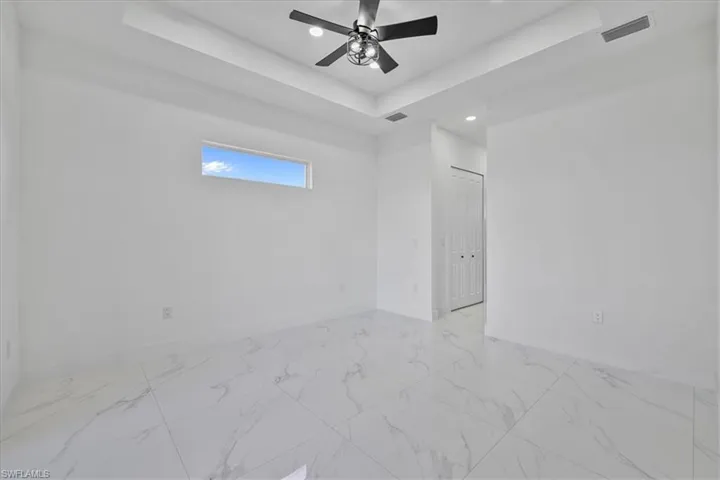 Unfurnished room featuring light marble finish flooring, a tray ceiling, a ceiling fan, and recessed lighting