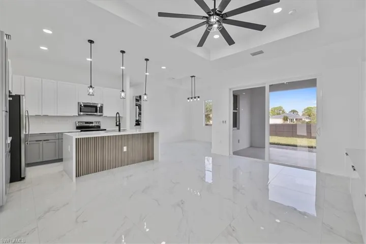 Kitchen featuring stainless steel appliances, light stone countertops, an island with sink, white cabinetry, and pendant lighting