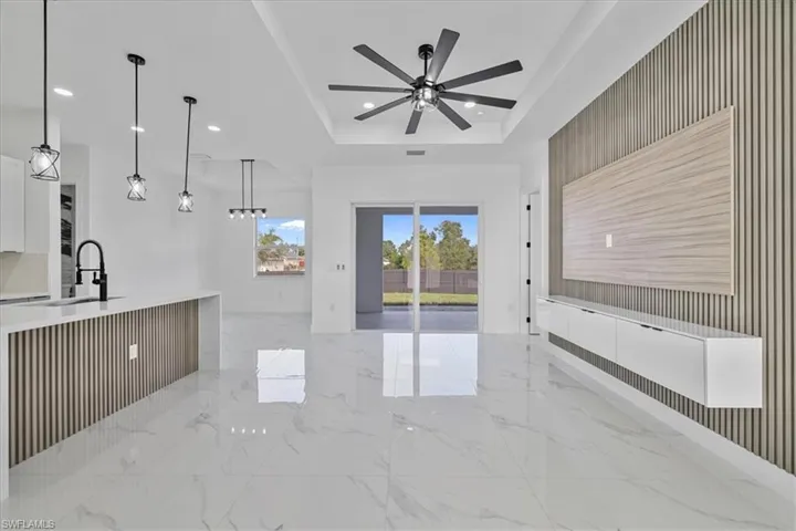 Unfurnished living room featuring a tray ceiling, recessed lighting, light marble finish floors, and ceiling fan