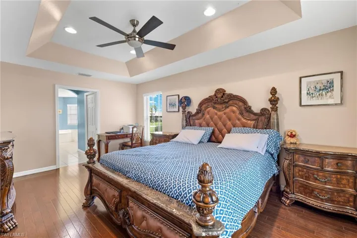 Bedroom with ceiling fan, ensuite bathroom, hardwood / wood-style flooring, and a tray ceiling