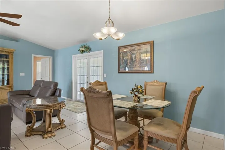 Tiled dining area with lofted ceiling, ceiling fan with notable chandelier, and french doors