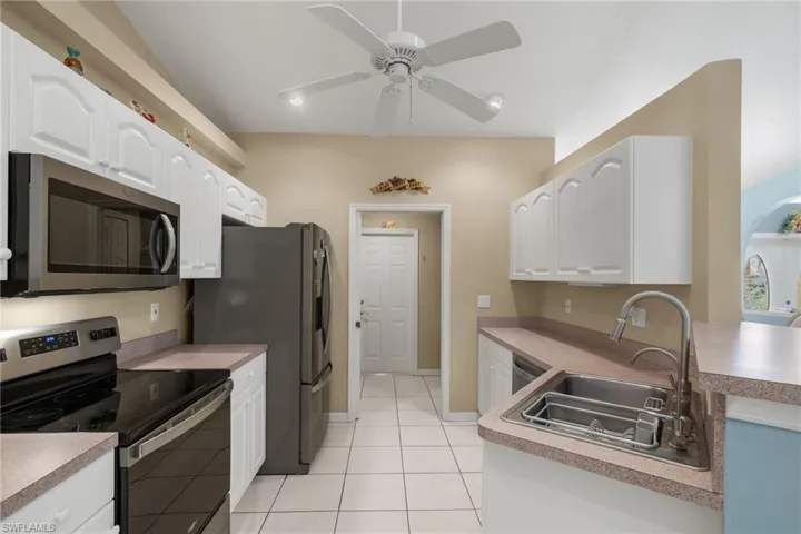 Kitchen featuring appliances with stainless steel finishes, white cabinets, sink, light tile patterned floors, and ceiling fan