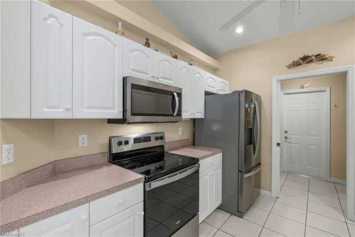 Kitchen with appliances with stainless steel finishes, light tile patterned flooring, white cabinets, and vaulted ceiling
