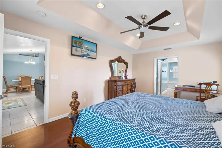 Bedroom featuring connected bathroom, hardwood / wood-style flooring, a raised ceiling, and ceiling fan