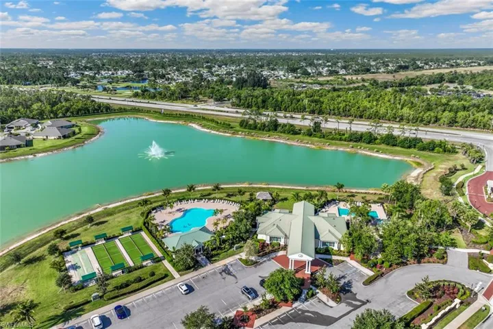 Aerial view showcasing the community lake with a fountain, a large swimming pool, and dedicated recreation courts