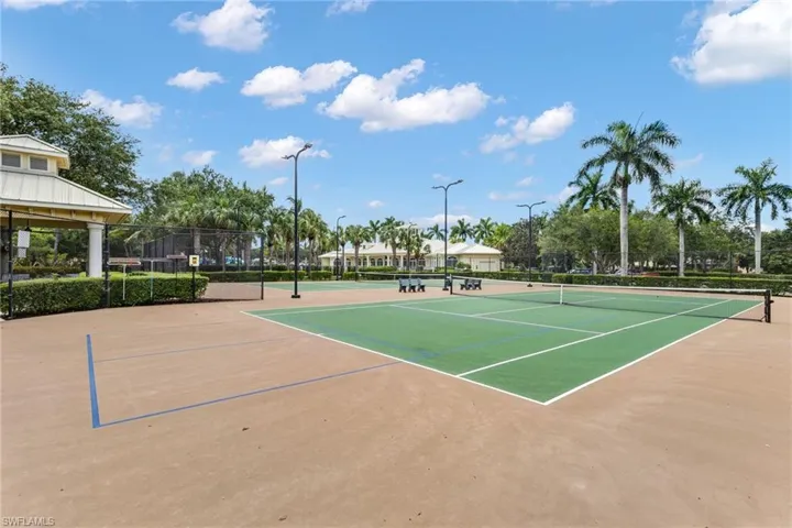 Tennis courts with a hard surface, surrounding landscaping, and permanent lighting fixtures