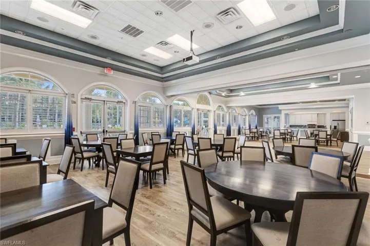 Sophisticated banquet hall featuring soaring ceilings with recessed lighting, expansive arched windows flooding the space with natural light, wood-finish flooring throughout, and multiple round dining tables with coordinating seating arrangements