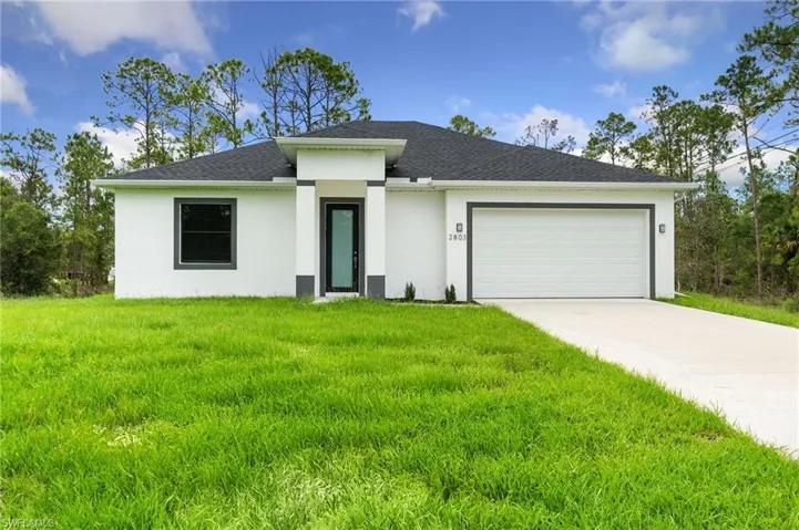 Prairie-style home featuring stucco siding, a front yard, a garage, concrete driveway, and roof with shingles