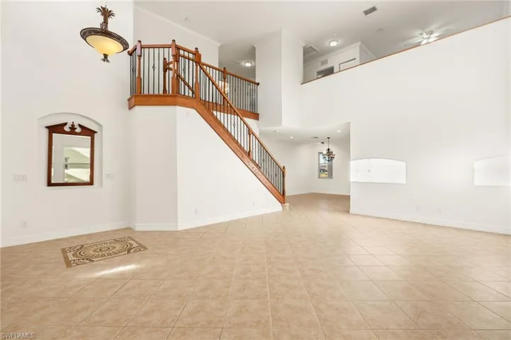 Unfurnished living room with a high ceiling, light tile patterned floors, ceiling fan, and crown molding