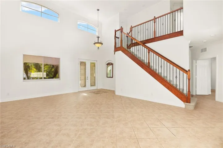 Unfurnished living room with french doors, a high ceiling, light tile patterned floors, and arched walkways