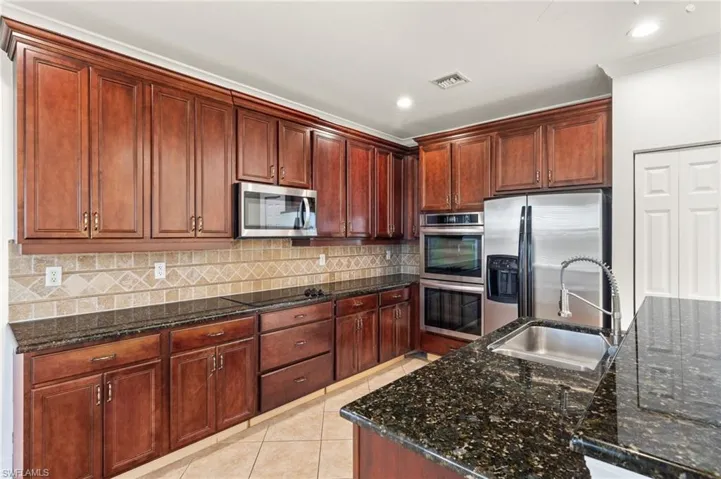 Kitchen featuring dark stone countertops, stainless steel appliances, backsplash, light tile patterned floors, and recessed lighting