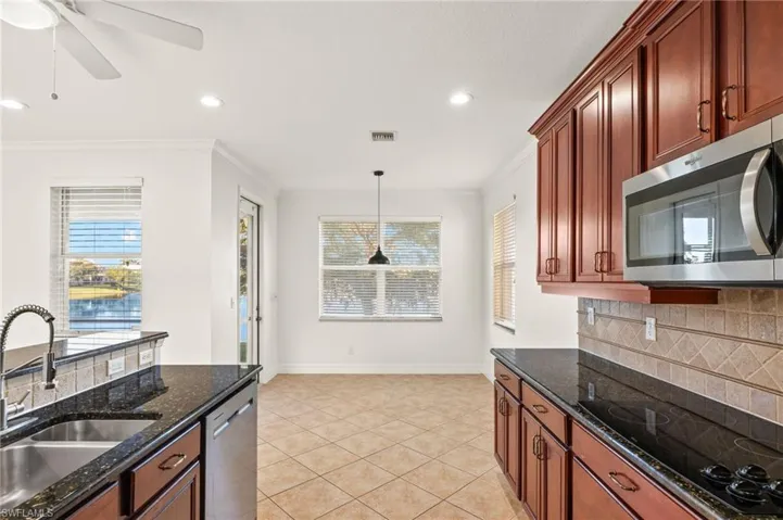 Kitchen with dark stone countertops, stainless steel appliances, decorative light fixtures, light tile patterned floors, and crown molding