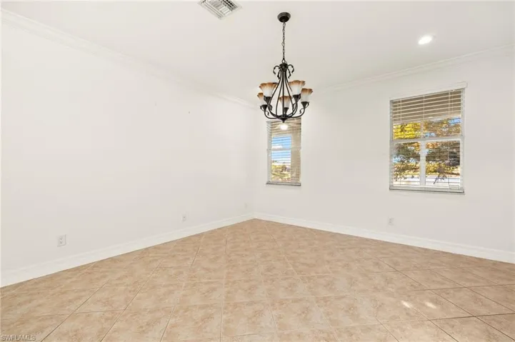Empty room with ornamental molding, hanging lights, and light tile patterned flooring