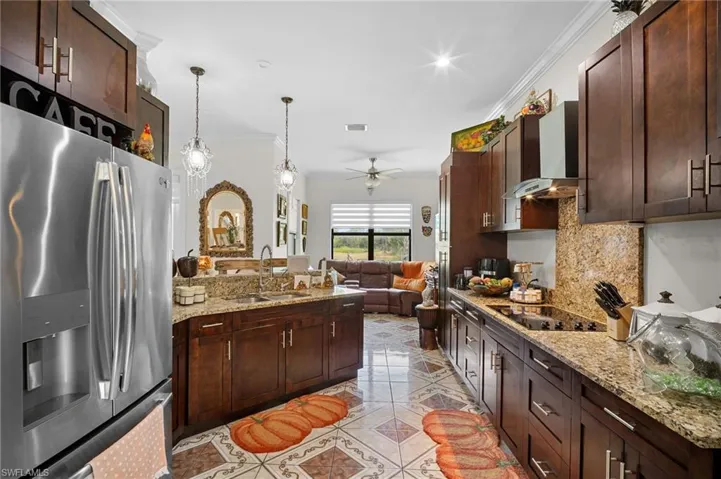 Kitchen with stainless steel fridge, dark brown cabinets, light stone counters, ornamental molding, and recessed lighting