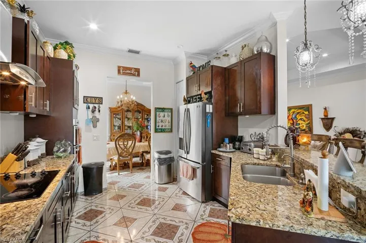 Kitchen featuring a chandelier, decorative light fixtures, stainless steel fridge with ice dispenser, light stone counters, and crown molding