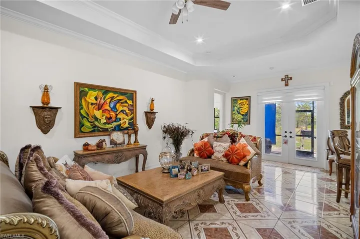 Tiled living room with ornamental molding, a raised ceiling, french doors, recessed lighting, and a ceiling fan