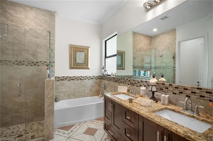 Full bathroom with crown molding, double vanity, a bath, tile walls, and a shower stall