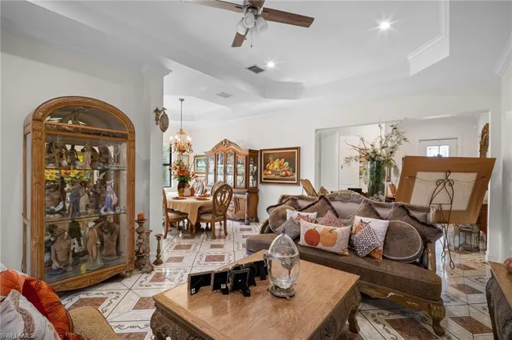 Living room featuring crown molding, a tray ceiling, ceiling fan, light tile patterned flooring, and a chandelier