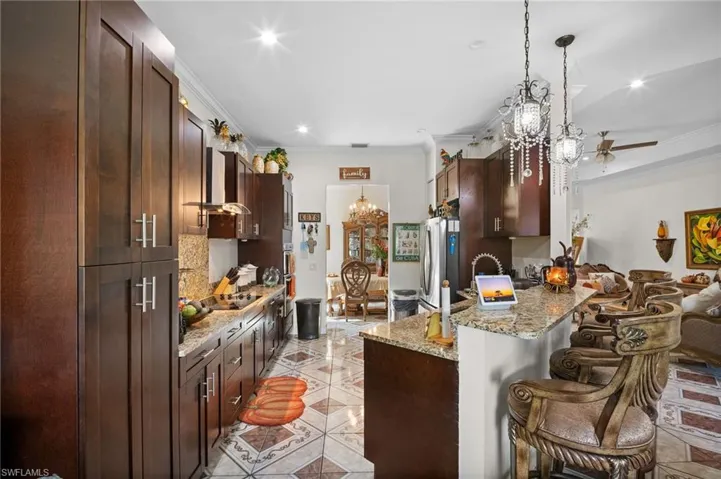 Kitchen with light stone countertops, dark brown cabinetry, crown molding, a breakfast bar, and pendant lighting