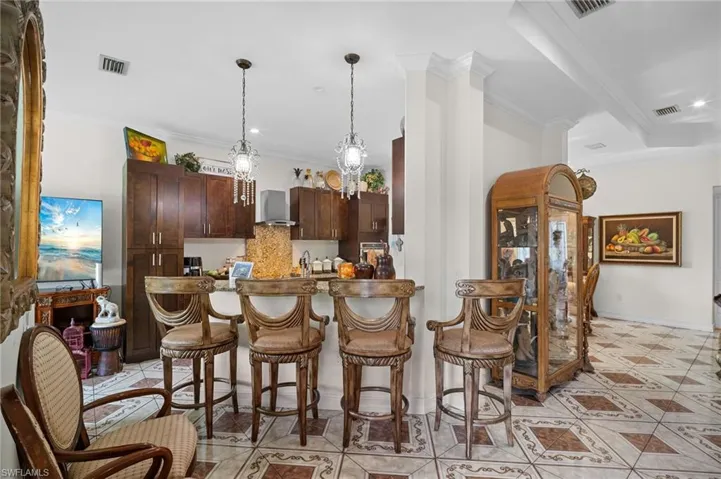 Kitchen with dark brown cabinetry, a kitchen bar, pendant lighting, ornamental molding, and a peninsula
