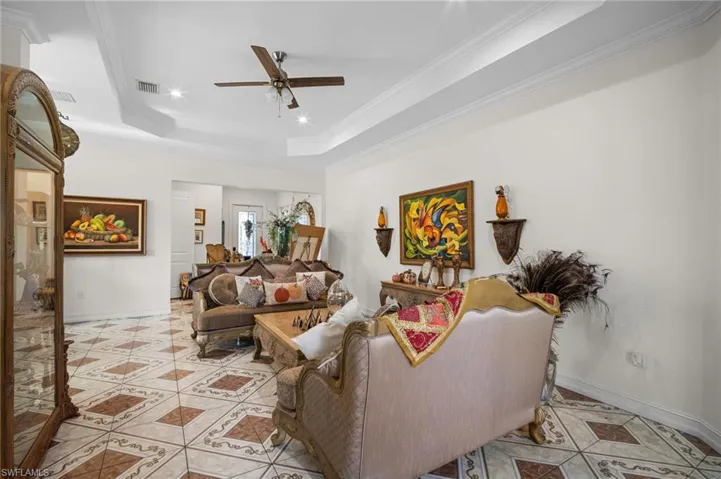 Living room with a raised ceiling, ornamental molding, a ceiling fan, light tile patterned flooring, and recessed lighting