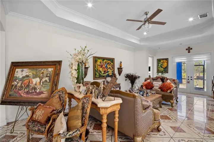 Living area with crown molding, a tray ceiling, french doors, light tile patterned flooring, and ceiling fan
