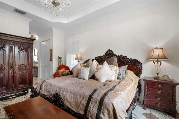 Bedroom with a tray ceiling, crown molding, a closet, a chandelier, and ensuite bath