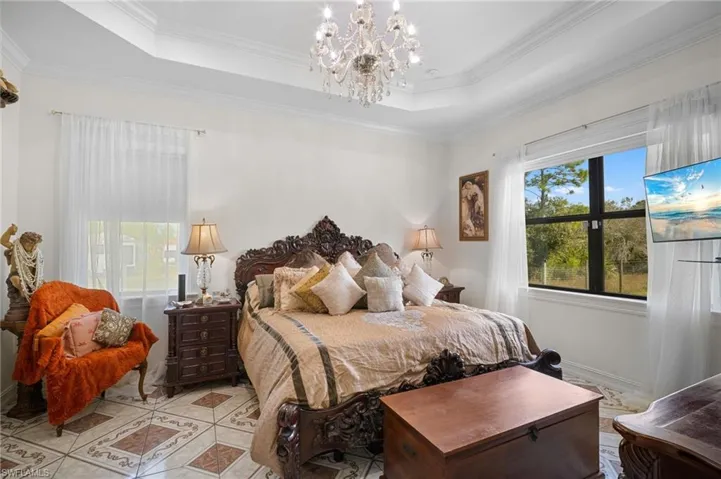 Tiled bedroom with a tray ceiling, ornamental molding, and a chandelier