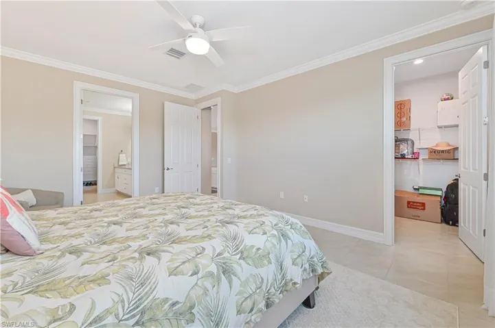 Bedroom featuring a spacious closet, ornamental molding, a ceiling fan, and light tile patterned flooring