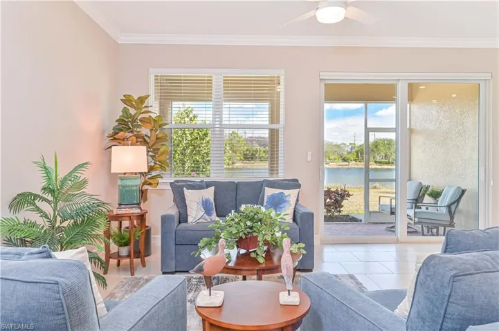 Tiled living room with ornamental molding, a water view, and a ceiling fan