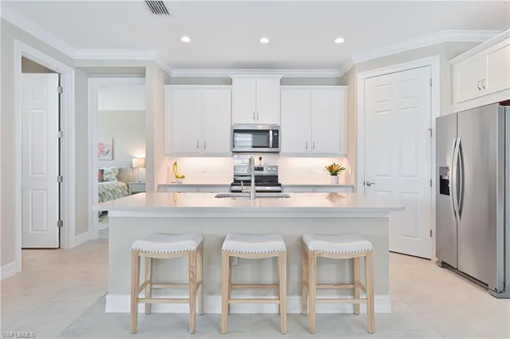 Kitchen featuring stainless steel appliances, white cabinetry, a kitchen bar, ornamental molding, and light stone countertops