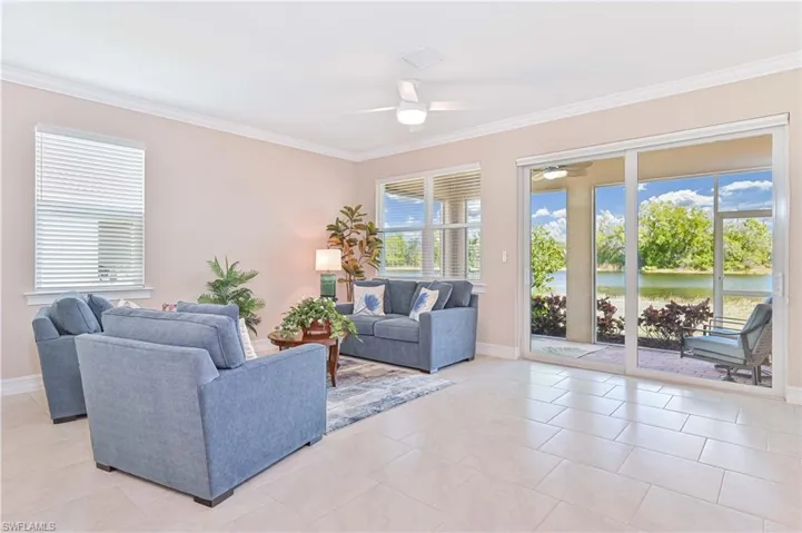 Living area with ceiling fan, a water view, ornamental molding, and light tile patterned flooring