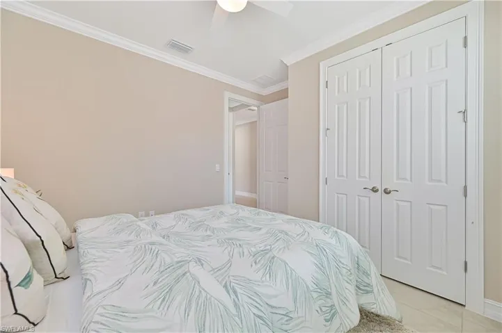 Bedroom with ornamental molding, ceiling fan, a closet, and tile patterned floors