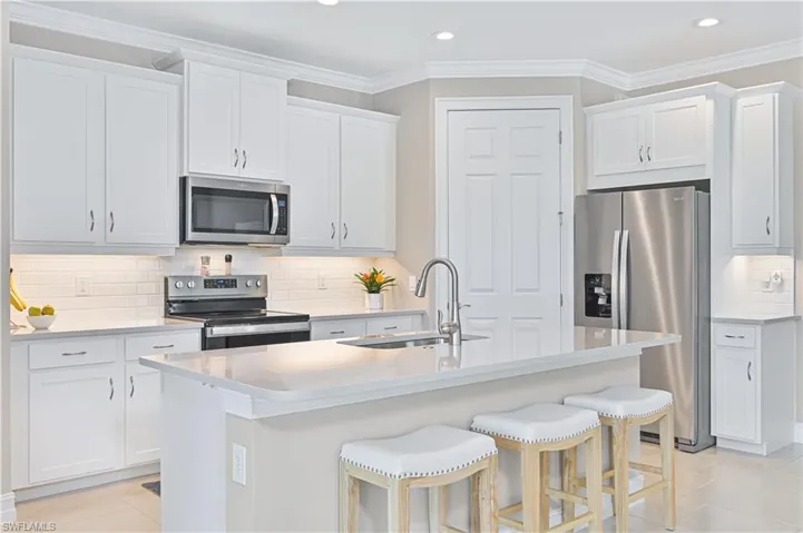 Kitchen with decorative backsplash, stainless steel appliances, light tile patterned floors, crown molding, and an island with sink