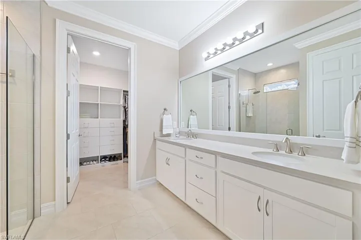 Bathroom featuring crown molding, double vanity, a stall shower, a walk in closet, and light tile patterned flooring