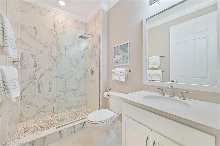 Bathroom featuring crown molding, vanity, and a marble finish shower